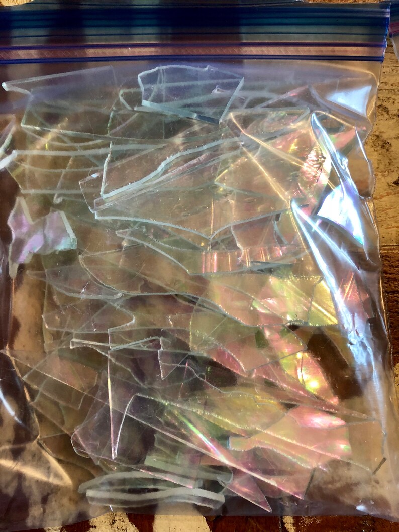 Puede incluir: Una bolsa de pl&aacute;stico transparente llena de trozos de vidrio iridiscente. Los fragmentos de vidrio son de varias formas y tama&ntilde;os, reflejando la luz con un brillo de arco&iacute;ris. La bolsa est&aacute; sellada con una cremallera azul y blanca.