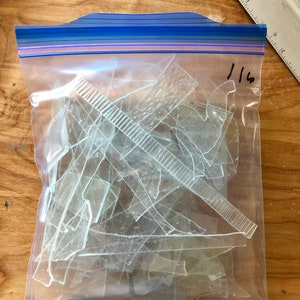 Puede incluir: Una bolsa de pl&aacute;stico transparente con cierre de cremallera azul llena de fragmentos de vidrio transparente de forma irregular. Una regla y el n&uacute;mero "116" son visibles en la bolsa. El contenido parece ser material de manualidades o para proyectos.