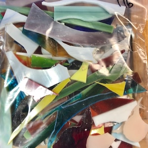 Puede incluir: Una bolsa de pl&aacute;stico transparente llena de coloridas piezas de mosaico de vidrio. Los fragmentos de vidrio son de varias formas y tama&ntilde;os, en tonos de blanco, verde, amarillo, azul y marr&oacute;n. El n&uacute;mero "116" est&aacute; escrito con un rotulador negro en la bolsa.