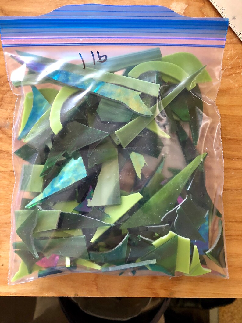 Puede incluir: Una bolsa de pl&aacute;stico transparente llena de trozos de vidrio verde de varios tonos. Los trozos de vidrio tienen formas irregulares, incluyendo tri&aacute;ngulos y piezas curvas. La bolsa est&aacute; etiquetada con el n&uacute;mero "1 lb" en rotulador negro.