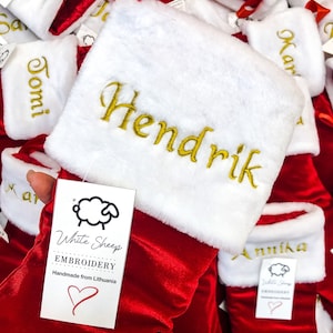 May include: Red velvet Christmas stockings with white faux fur cuffs, personalized with names in gold embroidery. The stockings are handmade in Lithuania by White Sheep Embroidery.