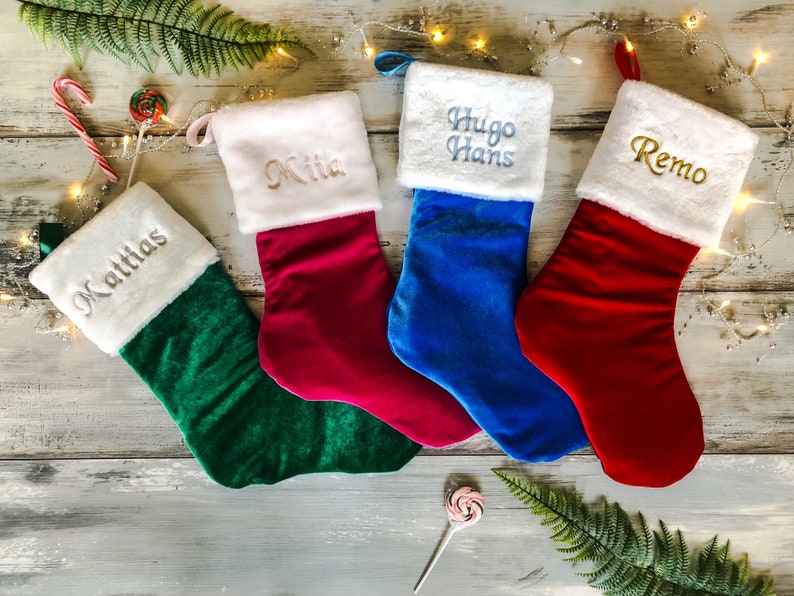 May include: Four personalized Christmas stockings with white fur trim. The stockings are green, red, blue, and pink. The names on the stockings are Matthias, Mia, Hugo Hans, and Remo.
