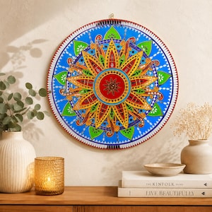 May include: A circular wall hanging featuring a vibrant mandala design with a central red sun motif, surrounded by layers of yellow, orange, green, and blue geometric patterns. The artwork includes reflective mirror accents and a red border.