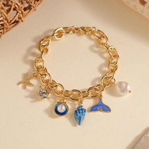 May include: Gold chain bracelet with multiple charms, including a starfish, a seashell, a pearl, and a blue whale tail.