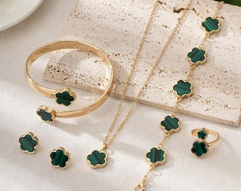May include: A gold jewelry set with green clover-shaped stones. The set includes a necklace, bracelet, earrings, and a ring.