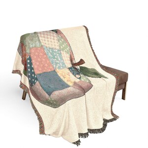 Peut inclure: Une couverture tissée avec un motif de pomme en patchwork dans les tons de vert, bleu, rose et crème. La couverture a une bordure à franges et est drapée sur un banc marron. Le motif de la pomme comprend une tige et une feuille.