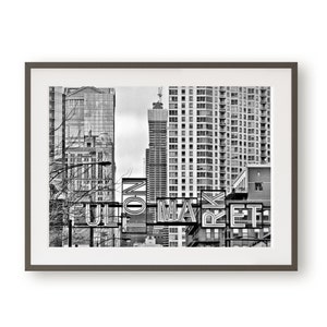 以下が含まれることがあります： ネオンの文字で「FULTON MARKET」と書かれた看板のある都市の風景の白黒写真。看板は尖った屋根のある高い建物の前にある。