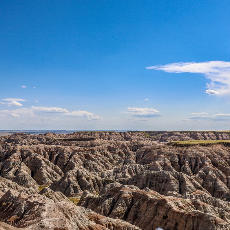 May include: A panoramic view of a vast, rugged landscape with a blue sky and white clouds. The terrain is characterized by numerous, eroded, and weathered rock formations, creating a dramatic and textured scene.