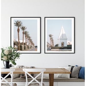 May include: Two framed prints of a white building with a pointed roof and palm trees in front of it. The building is on the left side of the image and the palm trees are on the right side of the image. The building is white and the palm trees are green. The sky is blue.