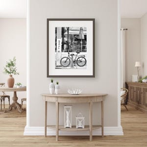 May include: Monochrome framed print featuring a bicycle parked on a street, with the text "Duval St" visible. The artwork hangs above a wooden console table, adorned with vases and candles.