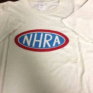 May include: White t-shirt with a red and blue oval logo that says "NHRA" in blue letters.