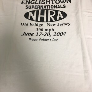 May include: White t-shirt with black text that reads "Feel the need for speed Englishtown Supernationals NHRA Old bridge New Jersey 300 mph June 17-20, 2004 Happy Father's Day"