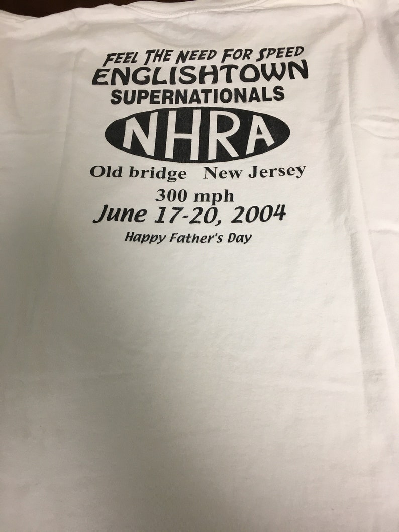May include: White t-shirt with black text that reads "Feel the need for speed Englishtown Supernationals NHRA Old bridge New Jersey 300 mph June 17-20, 2004 Happy Father's Day"