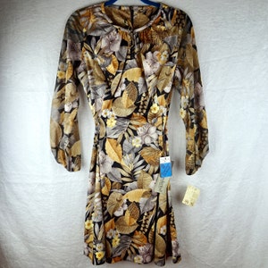 May include: A vintage dress with a floral pattern featuring large leaves and flowers in shades of brown, tan, gray, and yellow on a black background. The dress has long sleeves and a tie at the waist. A tag is attached.