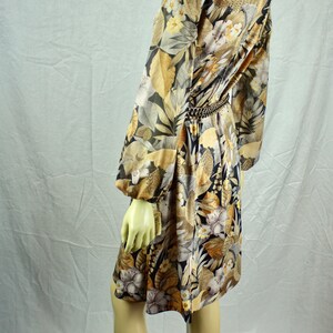 May include: A vintage dress with a floral pattern in shades of black, gold, and cream. The dress features long sleeves, a cinched waist with a gold chain belt, and a knee-length hemline. The dress is displayed on a mannequin.