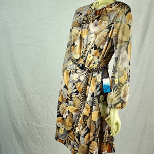 May include: A long-sleeved dress with a floral pattern in shades of brown, beige, and black. The dress features a tie neckline and a chain belt. The dress is displayed on a mannequin. The tag reads "Damce Dress".