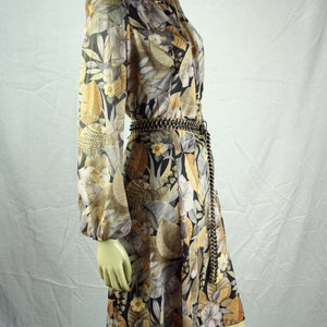 May include: A vintage-style dress with a floral pattern in shades of gold, black, and gray. The dress features long sleeves, a tie-neck detail, and a chain belt. The dress is knee-length.
