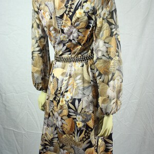 May include: A vintage dress with a botanical print in shades of brown, beige, and black. The long-sleeved dress features a floral pattern, a cinched waist with a chain belt, and a knee-length hemline. The dress is displayed on a mannequin.