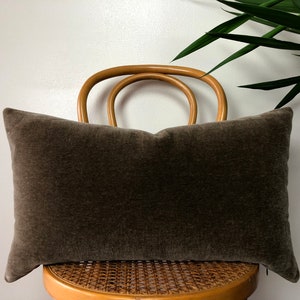 May include: A brown velvet lumbar pillow resting on a wooden chair with a woven seat.