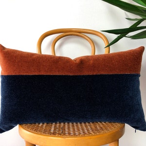 May include: A rectangular pillow with a two-tone design. The top half of the pillow is a burnt orange color, and the bottom half is a dark navy blue.