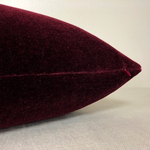 May include: A close-up of a burgundy velvet pillow with a zipper closure.