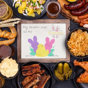 May include: A chalkboard sign with the text "My favorite peeps call me Momma" and a drawing of three yellow chicks with bunny ears. The sign is surrounded by various food items, including pretzels, radishes, sauerkraut, beer, and roasted chicken.