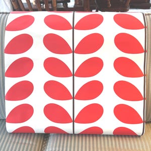 May include: A rectangular pillow with a white background and a repeating pattern of large, red teardrop shapes. The pillow has a black border and is resting on a striped sofa.