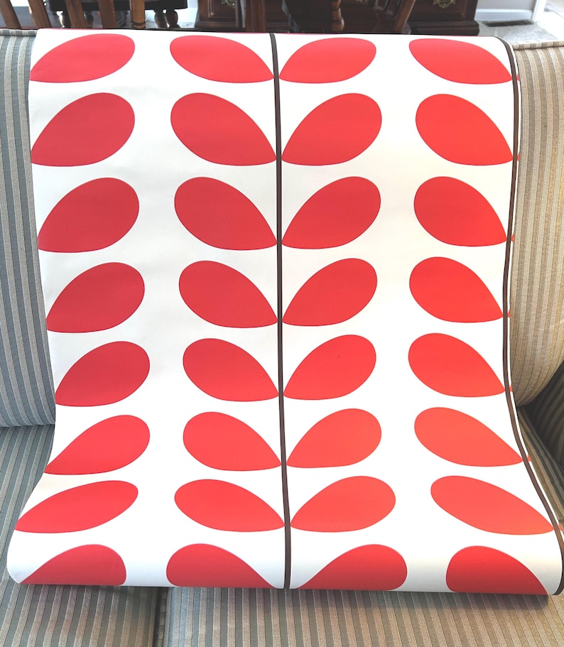 May include: Rolled wallpaper featuring a repeating pattern of red, teardrop-shaped designs on a white background. The design is divided by vertical black lines. The wallpaper is displayed on a striped upholstered chair.