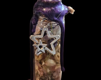 Peut inclure: Petite bouteille en verre remplie d'herbes et d'épices séchées, scellée avec de la cire violette et un charm en forme d'étoile argentée. La bouteille a un aspect rustique et artisanal, sur fond sombre.