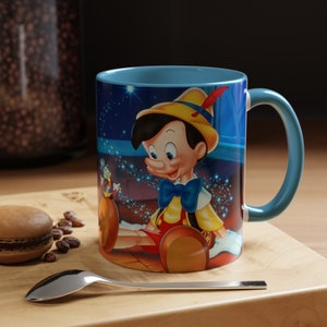 May include: A ceramic mug with a vibrant Pinocchio design. The mug has a light blue interior and handle, and the exterior features Pinocchio in a yellow hat and blue bow tie. The background includes stars and a magical scene.