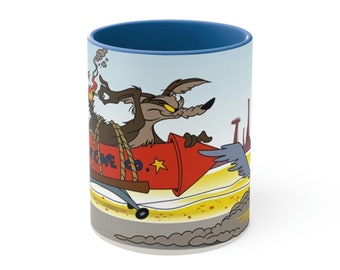 May include: A white ceramic mug with a blue rim features a cartoon coyote riding a red rocket with the text "ACME CO." on the side. The coyote has a determined expression and is flying through the air with smoke trails behind the rocket.