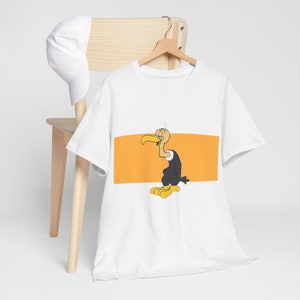 May include: White t-shirt with a cartoon image of a black vulture with a yellow beak and feet. The vulture is standing on a yellow rectangle.