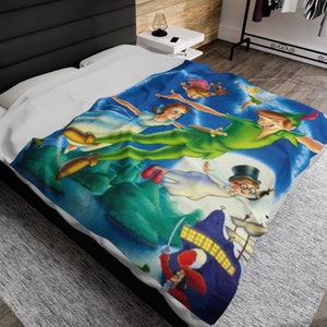 May include: A blue blanket with a colourful illustration of Peter Pan and other characters flying over Neverland. The design includes Peter Pan in a green outfit, Wendy, John, Michael, and Captain Hook's ship. The blanket is spread on a bed.