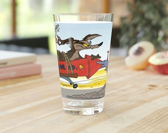 May include: A glass featuring a cartoon image of Wile E. Coyote riding a rocket with the text "ACME CO." printed on the side. The background is a blue sky with clouds.