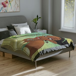 May include: A colorful blanket featuring a cartoon illustration of a woman with brown skin, black hair, and a green and yellow floral design. The blanket is draped over a gray bed.