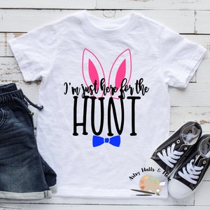 Peut inclure: T-shirt blanc avec des oreilles de lapin roses et un nœud papillon bleu. Le texte sur le t-shirt est "I'm just here for the HUNT".