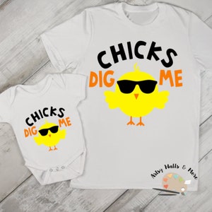 Peut inclure: Deux t-shirts blancs avec un poussin jaune portant des lunettes de soleil et le texte "CHICKS DIG ME". Le plus petit t-shirt est un body pour bébé.