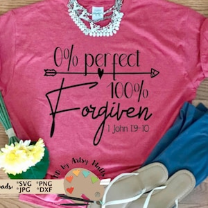 Könnte beinhalten: Ein pinkfarbenes T-Shirt mit dem Text "0% perfekt 100% Vergeben 1 Johannes 1:9-10" in schwarzer Schrift. Der Text ist mittig auf dem Shirt platziert und von einem kleinen Pfeil nach rechts umgeben.