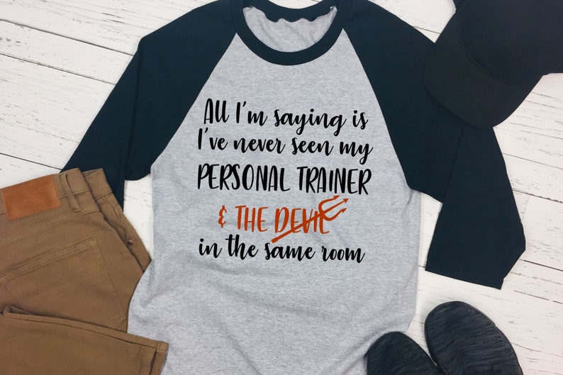 May include: A gray and black baseball tee shirt with the text "All I'm saying is I've never seen my PERSONAL TRAINER & THE DEVIL in the same room".