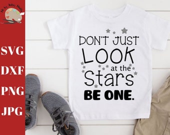 May include: White t-shirt with the text "DON'T JUST LOOK at the Stars BE ONE" in black. Gray stars are scattered around the text. Gray sneakers and khaki shorts are visible.