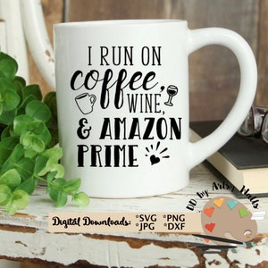 May include: White coffee mug with black text that reads "I run on coffee, wine, & Amazon Prime". The mug has a black coffee cup and wine glass icon. The mug is sitting on a wooden surface with a green plant and a book with glasses on top.
