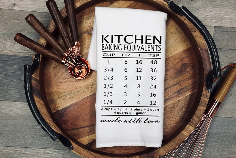 May include: White kitchen tea towel with black text that reads "Kitchen Baking Equivalents" and a chart showing cup, ounce, tablespoon, and teaspoon conversions. The text at the bottom reads "made with love".