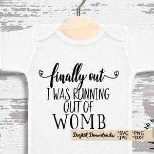 May include: White baby onesie with the text "finally out I WAS RUNNING OUT OF WOMB" in black script. The onesie is hanging on a wooden hanger. The design includes heart accents.