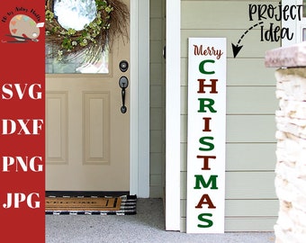 May include: A white wooden sign with the words "Merry Christmas" in red and green letters. The sign is leaning against a brick wall and a door with a wreath.