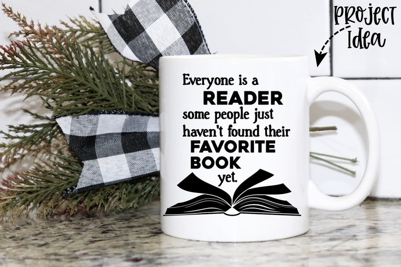 May include: White ceramic mug with a black design that reads "Everyone is a READER some people just haven't found their FAVORITE BOOK yet."  The mug is sitting on a table with a black and white checkered ribbon and a green plant.