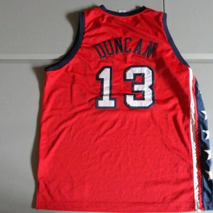 May include: Red basketball jersey with white and blue trim. The back of the jersey has the name "Duncan" and the number "13" in white.