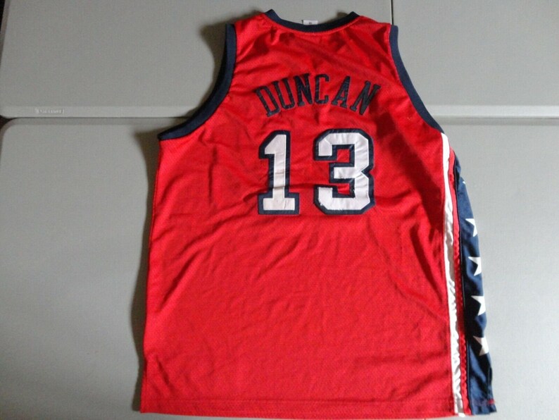 May include: Red basketball jersey with white and blue trim. The back of the jersey has the name "Duncan" and the number "13" in white.