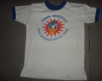 May include: White t-shirt with a blue ringer neck and a red, white, and blue graphic of Donald Duck with the text "Happy Birthday 1934-Donald Duck-1984".