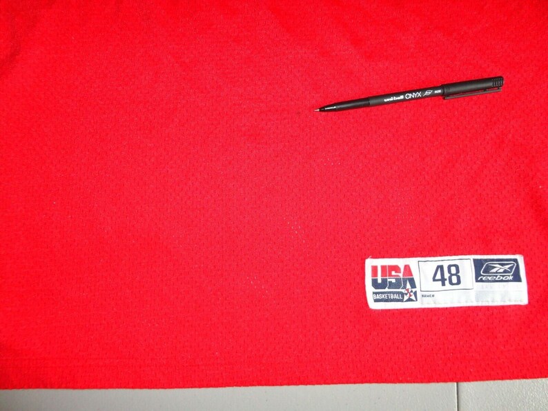 May include: Red basketball jersey with a white Reebok patch that says "USA Basketball" and "48" on it.