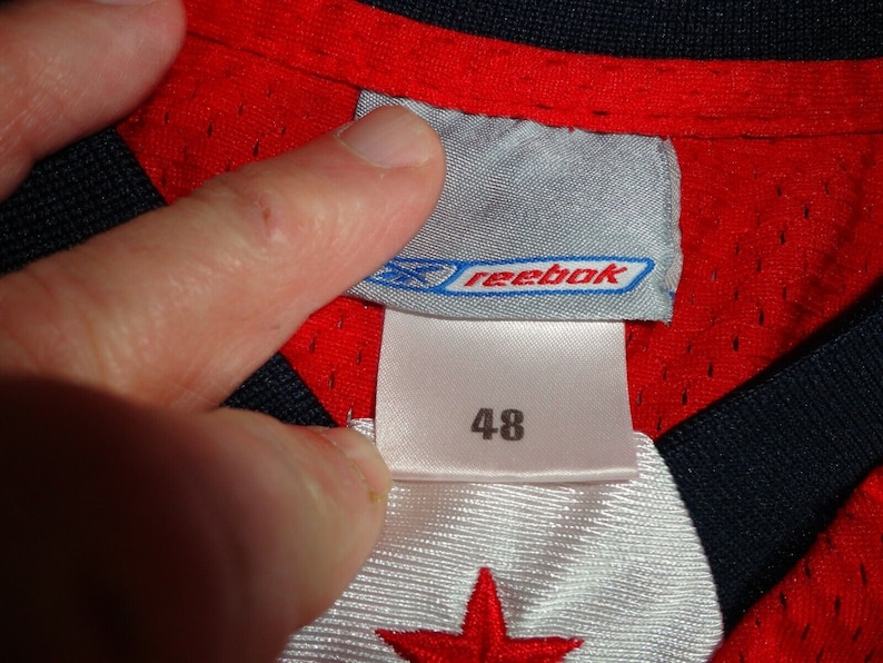 May include: Red and black Reebok jersey with a white star on the front. The jersey has a size tag that says "48" and "Reebok".